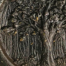 Load image into Gallery viewer, An extreme close-up view of grey face soap with an embossed tree design, and embedded black specks of charcoal and small, brown pieces of hemp that can be seen.
